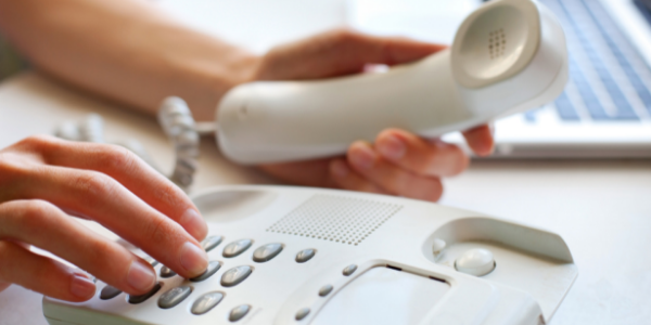 call hands dialing a white corded phone with open laptop in the background